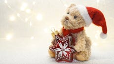 一只可爱的泰迪熊戴着圣诞帽，手里拿着星形圣诞装饰，背景里灯光闪烁