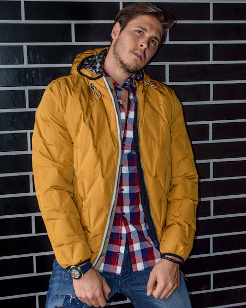 Free Man Wearing Yellow Zip-up Jacket Leaning on Brown Brick Wall Stock Photo