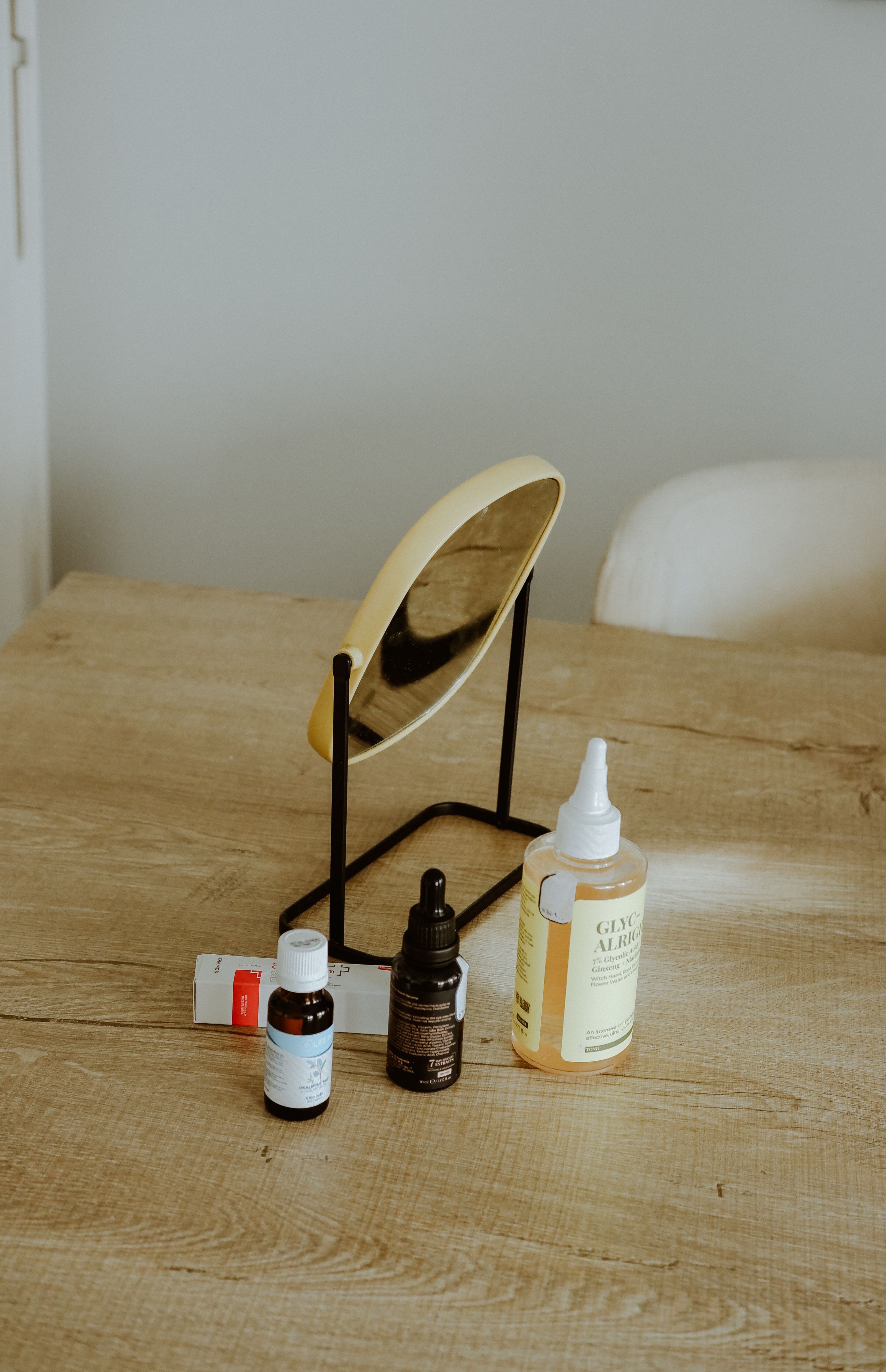 Uma seleção de produtos para a pele e um espelho sobre uma mesa de madeira.