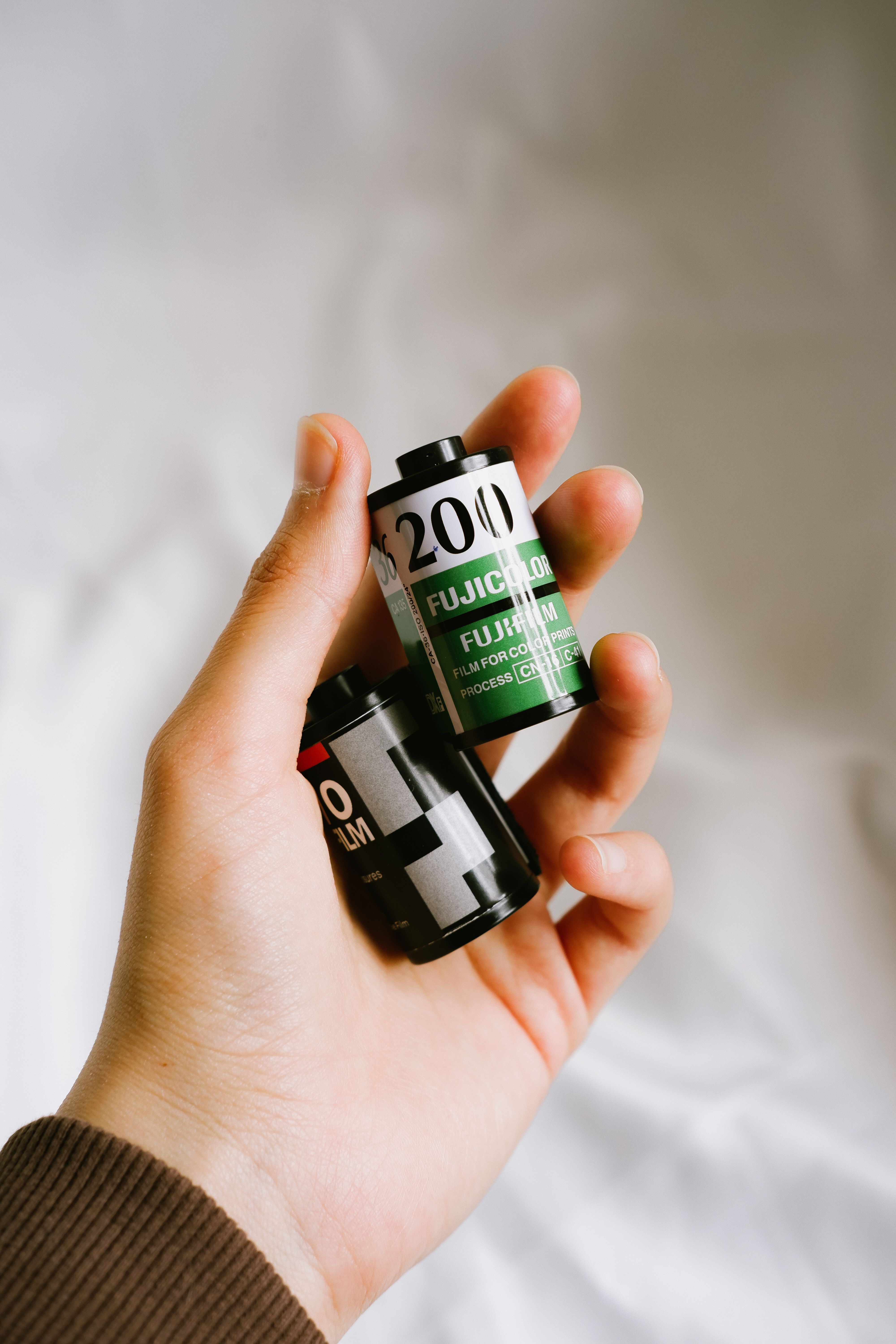 A close-up shot of a hand holding two Fujicolor film rolls with a soft background.