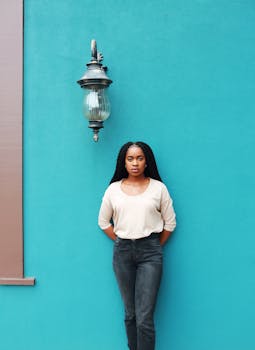 A fashionable woman poses confidently against a vibrant turquoise wall outdoors.