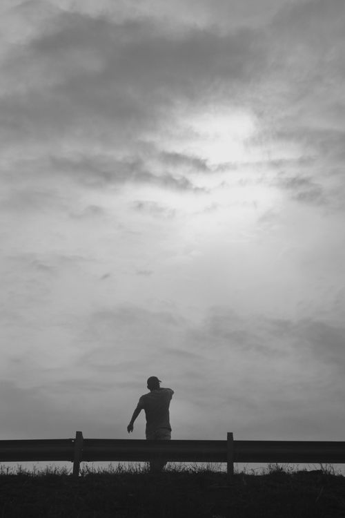 Free A black and white silhouette of a person standing against a cloudy sky creating a dramatic mood. Stock Photo
