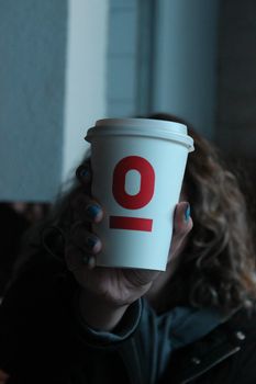 Focused image of a hand holding a coffee cup with red letters in a dimly lit setting.