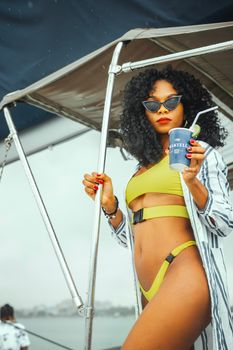 A fashionable woman in a green bikini holding a drink onboard a boat in Dar es Salaam.