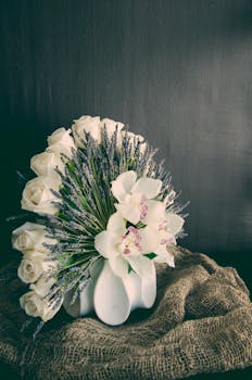 粗麻布花瓶里插着一束精致的白玫瑰、兰花与熏衣草