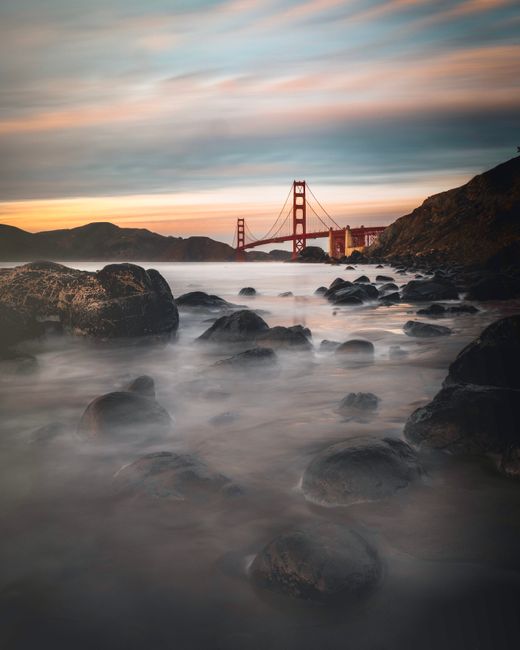 Scenic view of the Golden Gate Bridge at dusk with misty waves and rocks in San Francisco.