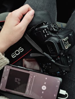 Close-up of a woman holding a DSLR camera and a smartphone playing music. Perfect for tech and lifestyle themes.