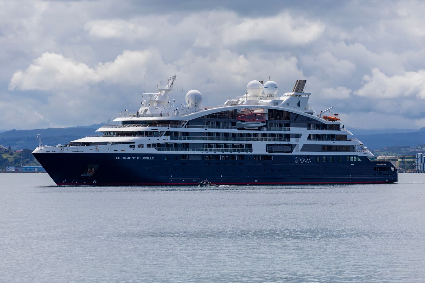 Ponant's expedition yacht Le Dumont-d'Urville under way on calm water beneath a cloudy sky