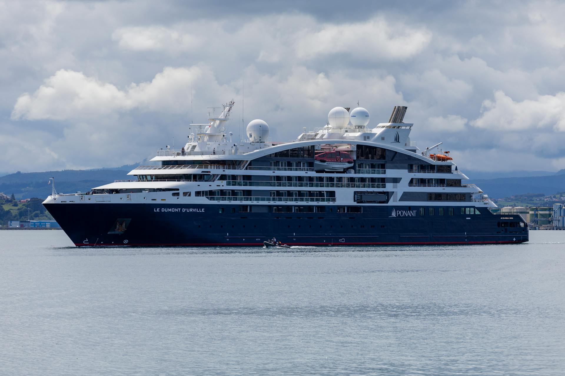 Elegant cruise ship Le Dumont D'Urville sailing on calm waters under cloudy skies.