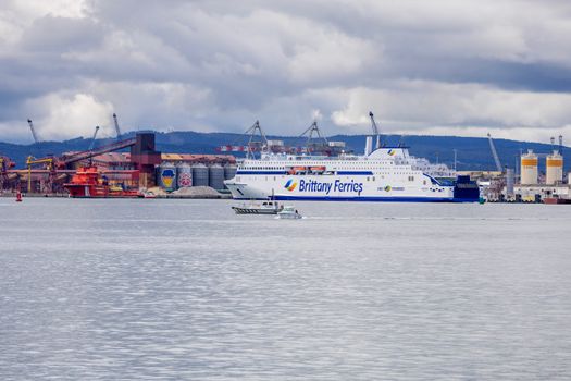 Brittany Ferries ship in a busy industrial harbor with cloudy skies.