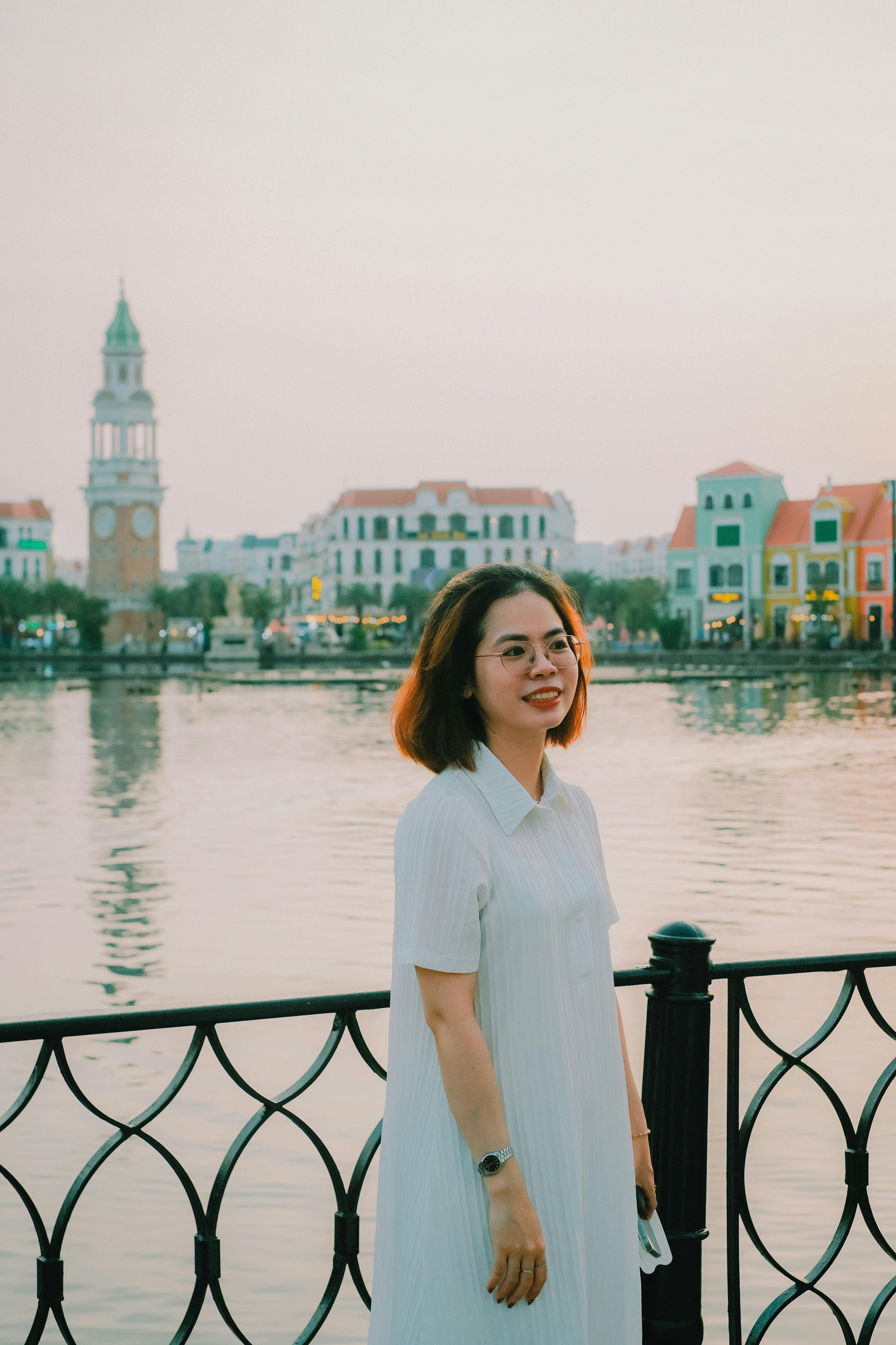 A young woman smiling by a waterfront with picturesque architecture in Vietnam.