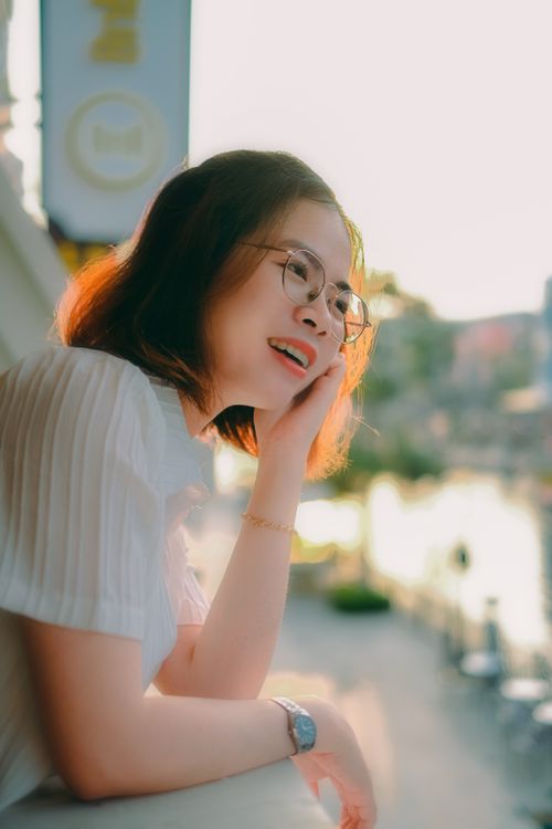 Free Portrait of a smiling woman with eyeglasses enjoying a sunset view from a city balcony. Stock Photo