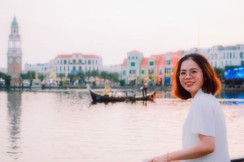 Free A young woman smiles by the water with colorful buildings and a gondola in Vietnam. Stock Photo