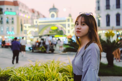Free Portrait of a young woman standing in a bustling cityscape with neon lights at dusk. Stock Photo