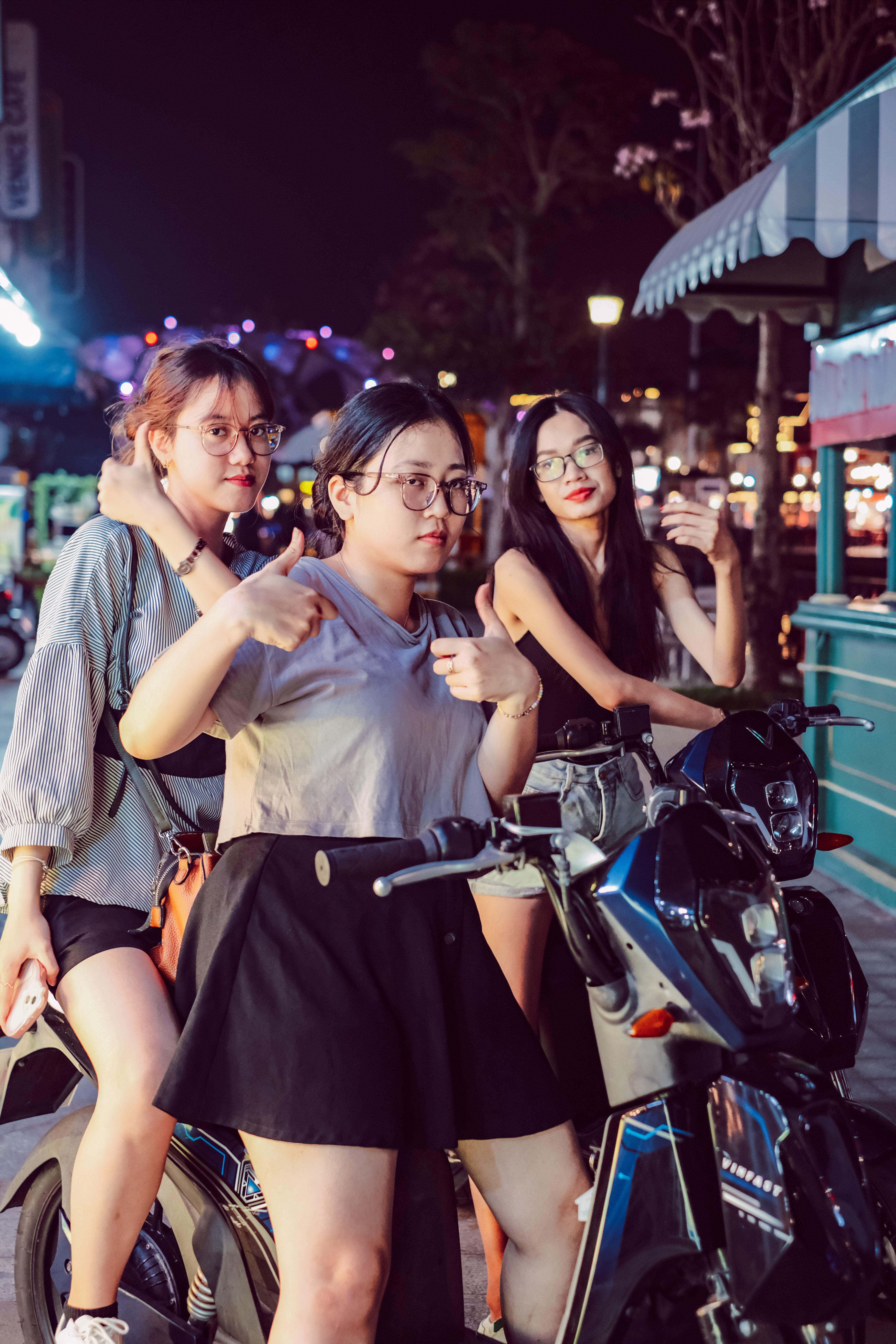 Three young women pose confidently on scooters, embracing city nightlife elegance.