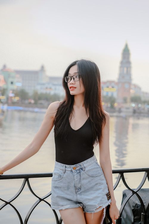 Free Stylish young woman poses by a scenic waterfront railing during summer. Stock Photo