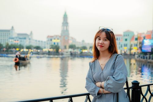 Free A young woman standing by a scenic waterfront in a vibrant town, smiling confidently. Stock Photo