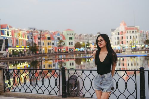 Free A fashionable young woman poses by a vibrant urban backdrop with colorful reflections in the water. Stock Photo
