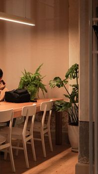 A warm and cozy indoor seating area featuring white chairs, a wooden table, and lush greenery.