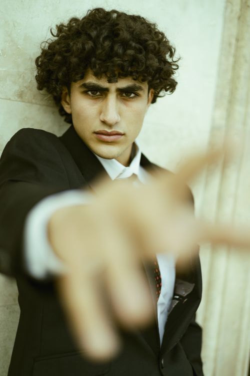 Free A focused young man in a black suit extends his hand towards the camera, creating a dynamic and compelling portrait. Stock Photo