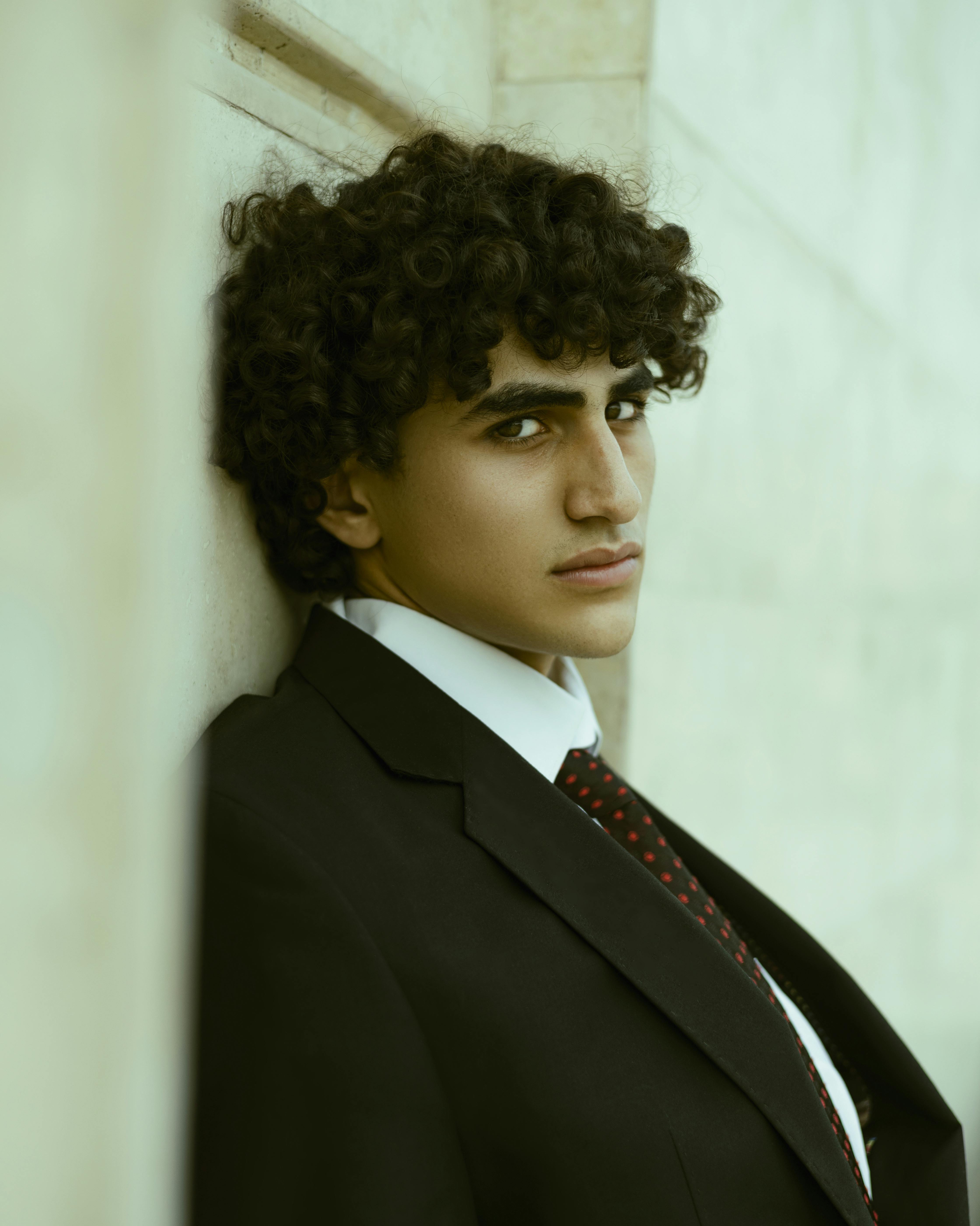 Portrait of a young man with curly hair in a suit against a white background.