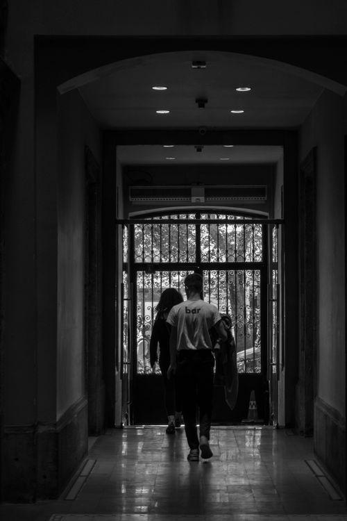 Free Black and white image of people walking towards a gate in a corridor, providing a classic and moody atmosphere. Stock Photo