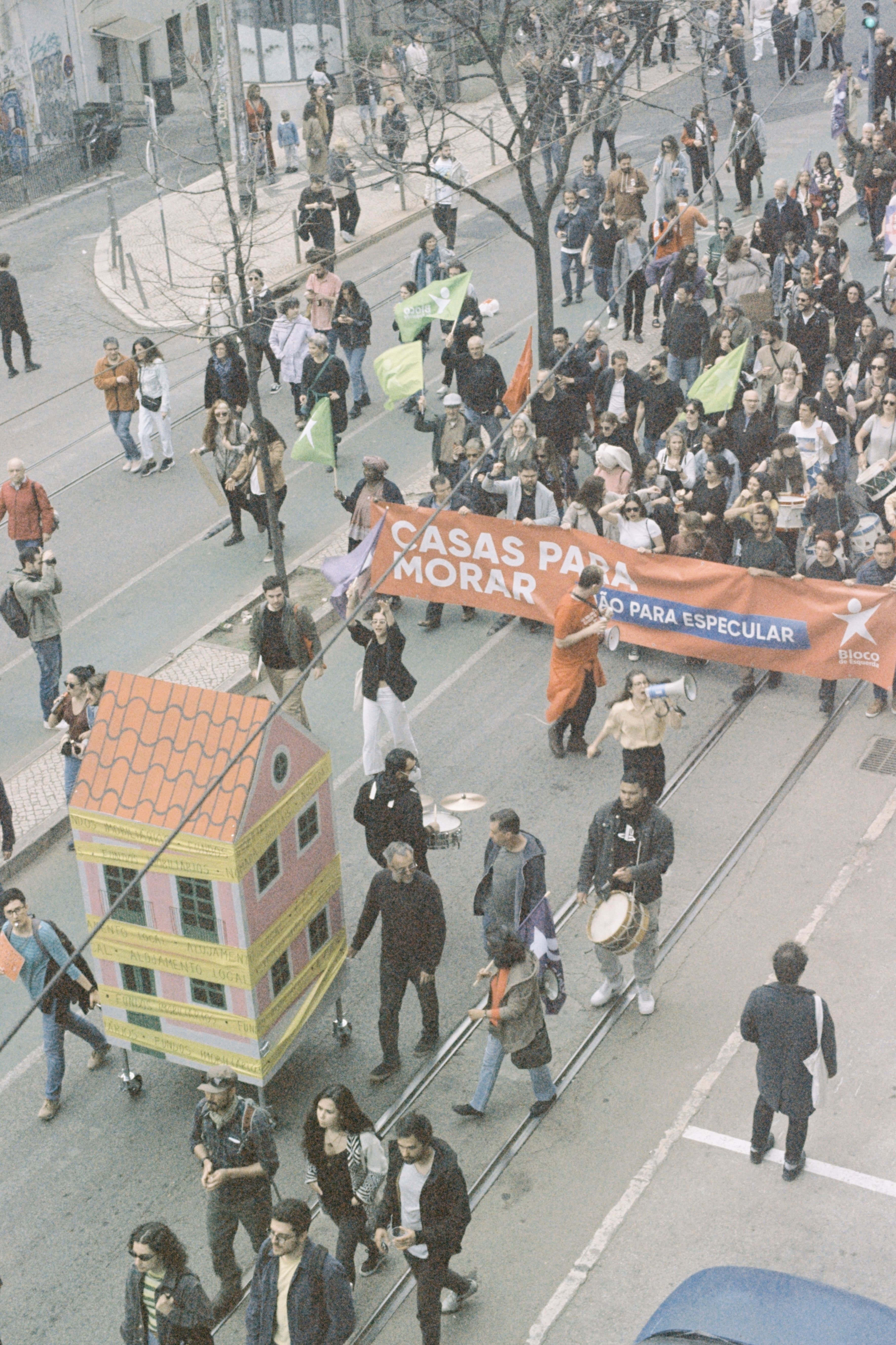 Aerial view of a protest in Lisbon with people carrying banners about housing rights.