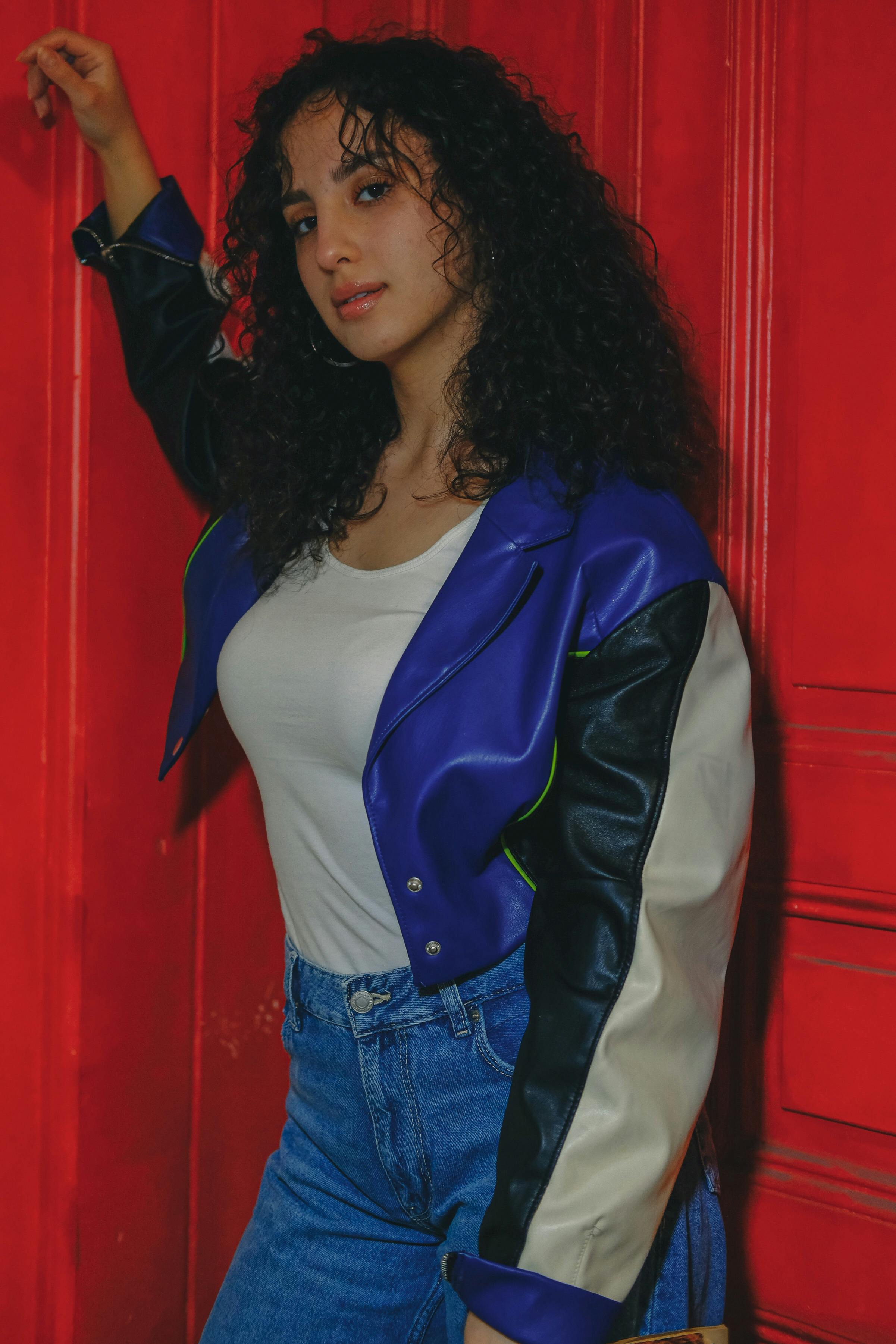 a woman in jeans and a leather jacket standing next to a red door