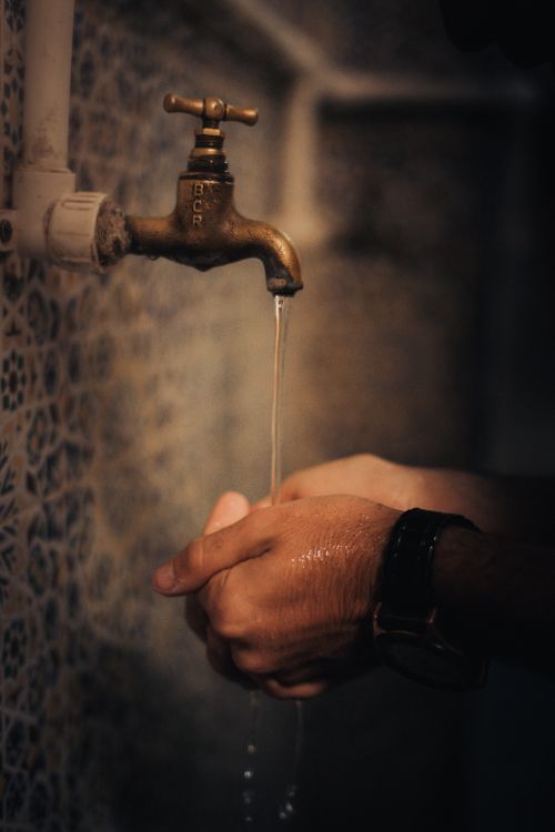 Free Close-up of hands washing under a vintage tap with water dripping in a dimly lit space. Stock Photo