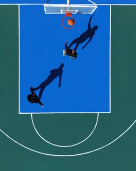 Aerial shot of two men playing basketball on a vibrant court, casting shadows.
