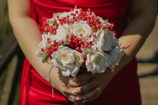 A close-up of a bouquet with white roses and red berries, held by a woman in a red dress.