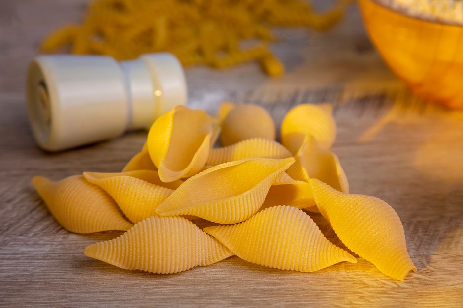 Fotomural Una toma detallada de pasta conchiglie cruda sobre una mesa de madera con un molinillo de pimienta.