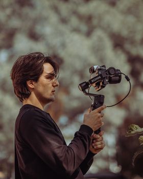 Young man using a Ronin gimbal stabilizer for filming, set in a natural outdoor environment.