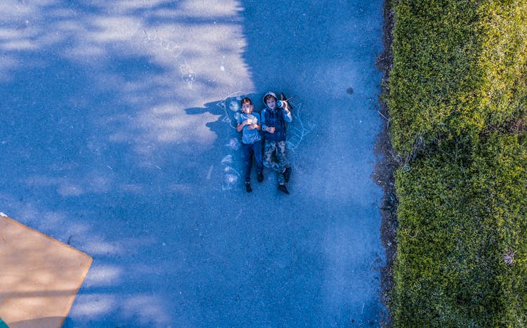 Photo Of Two Person Lying On Road Near Green Grass Field