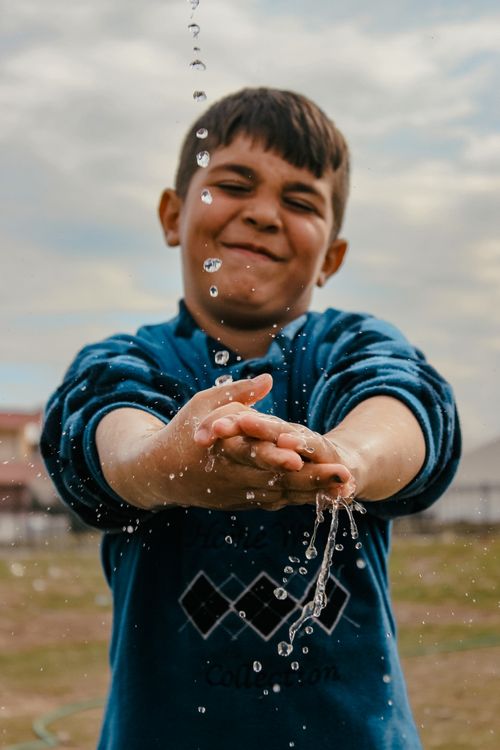 Free Joyful young boy having fun splashing water outdoors on a sunny day. Stock Photo