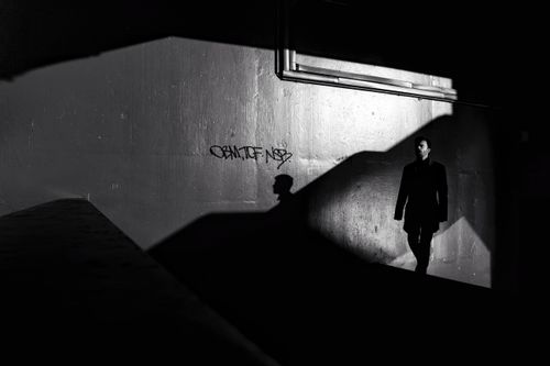 Free A solitary figure casts a dramatic shadow on an urban wall in black and white, creating a moody atmosphere. Stock Photo