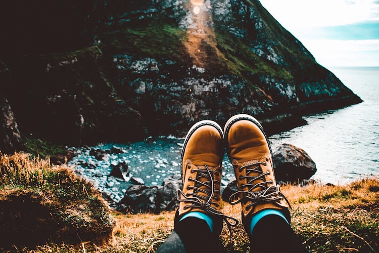 Person Wearing Pair Of Brown Suede Work Boots Facing Body Of Water