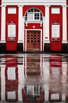 红色建筑立面有一扇木制门，倒影映在潮湿的街道上