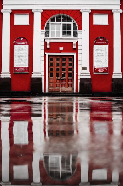 Red building facade with a wooden door and its reflection in a wet street.