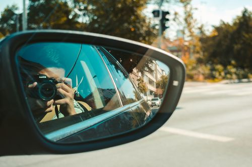 Free Candid shot of a photographer capturing a moment through a car's side mirror on a bright day. Stock Photo
