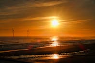 宁静的海滩上，迷人的日出映衬着风力涡轮机的轮廓，天空一片金黄