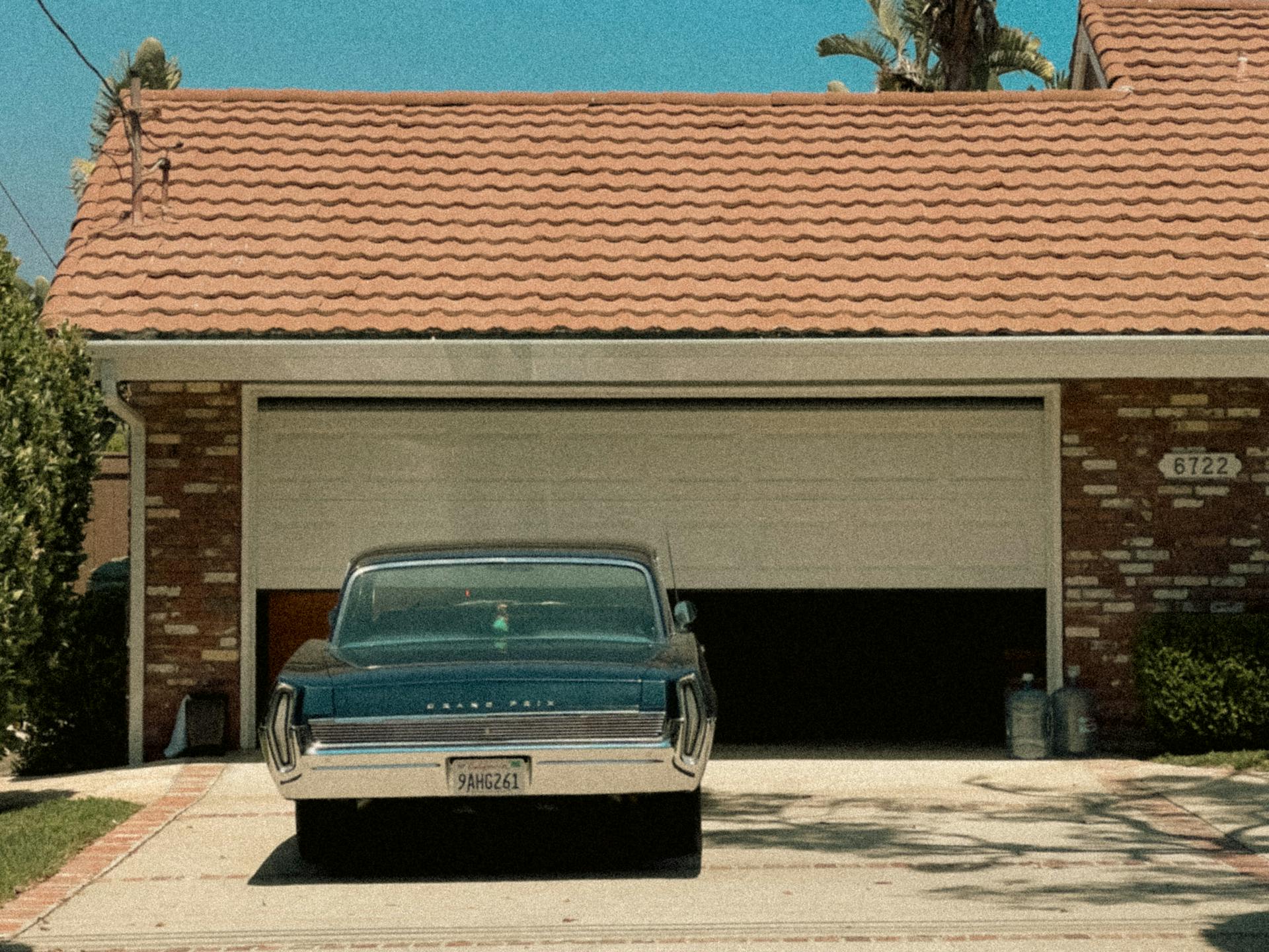 A classic muscle car parked in front of a stylish Malibu garage on a sunny day.