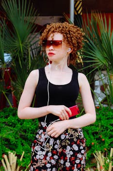 一位卷发、戴着太阳镜和红色智能手机的白化病妇女正在户外听音乐