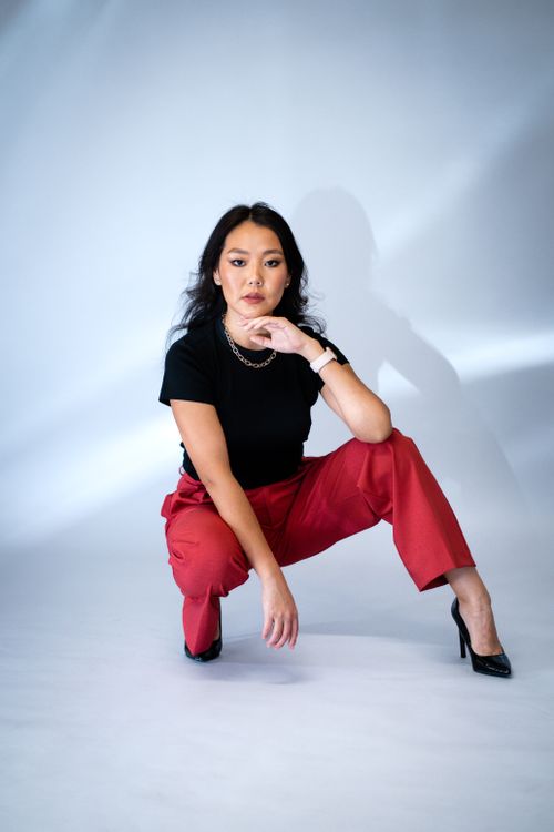 Free Fashion portrait of a stylish woman crouching in red pants and black top against a gray background. Stock Photo