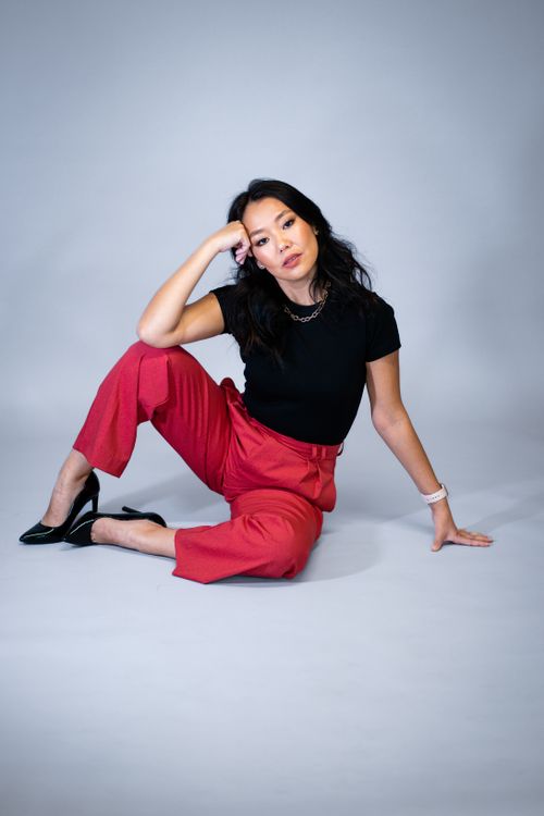 Free Chic fashion portrait of a woman in red pants and black blouse posing elegantly in a studio setting. Stock Photo