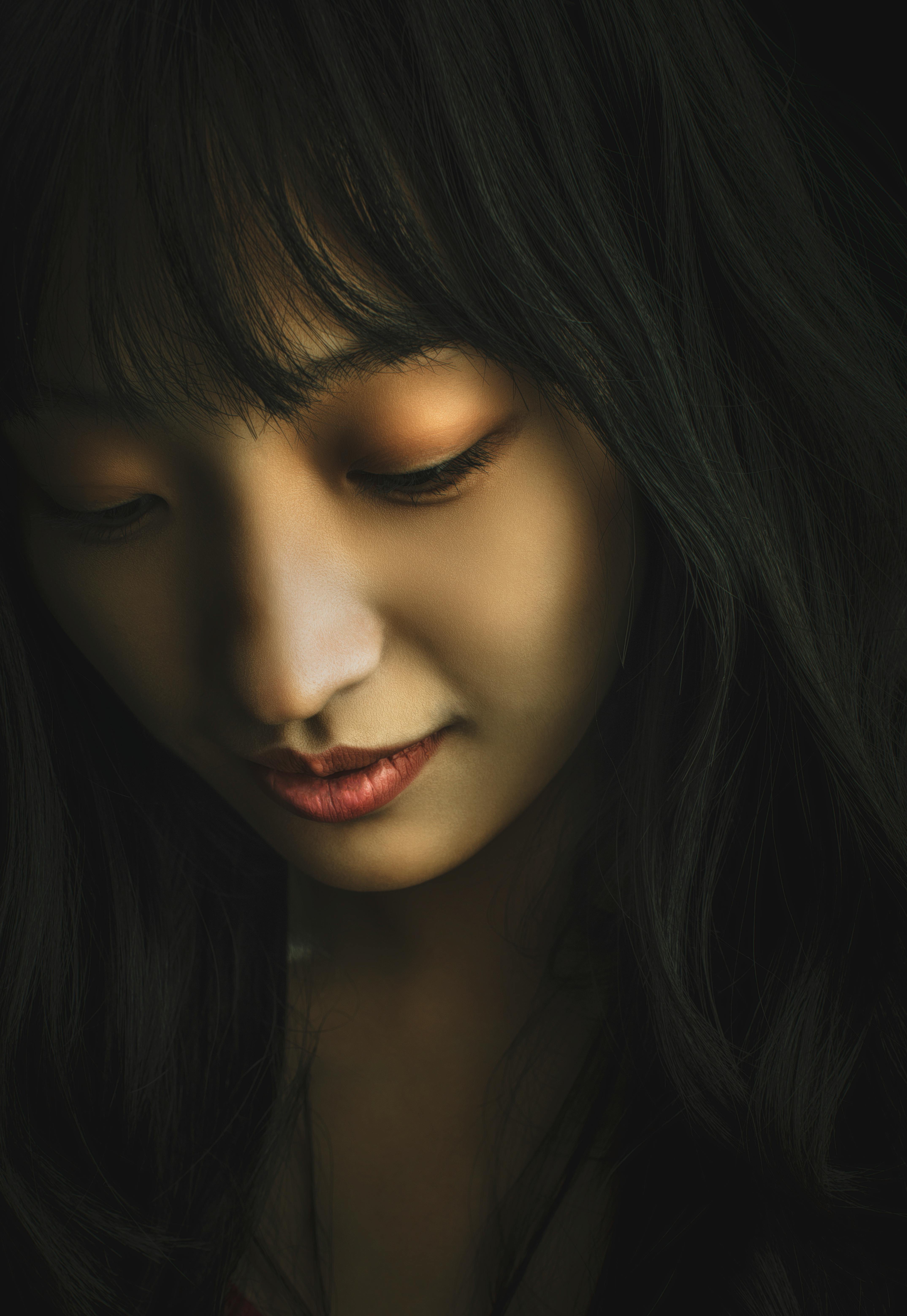 Close-up portrait of an Asian woman with a serene expression and long dark hair, looking down.