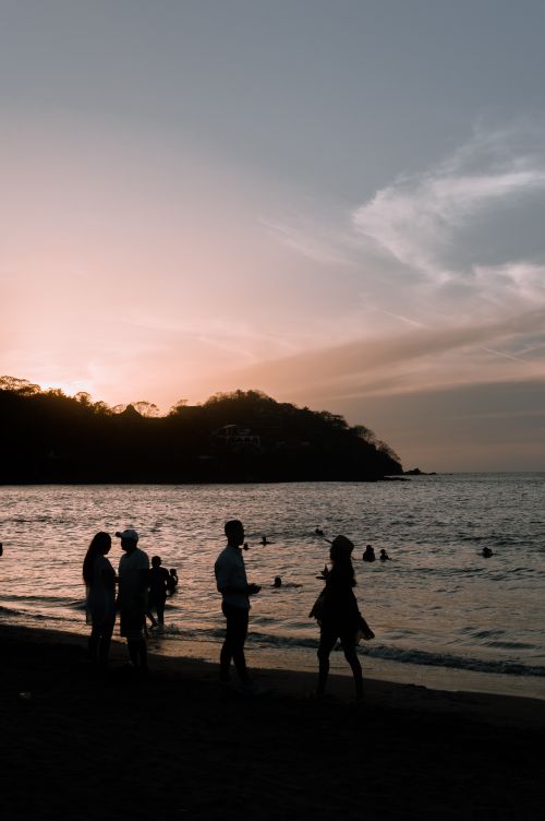 Free People enjoying a peaceful sunset at the beach with silhouettes against a serene ocean backdrop. Stock Photo