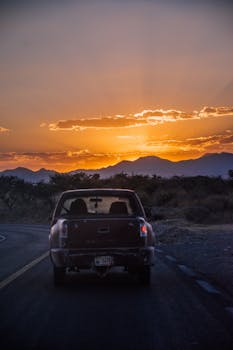 A pickup truck drives along a winding road during a vibrant sunset in Guanajuato, Mexico.