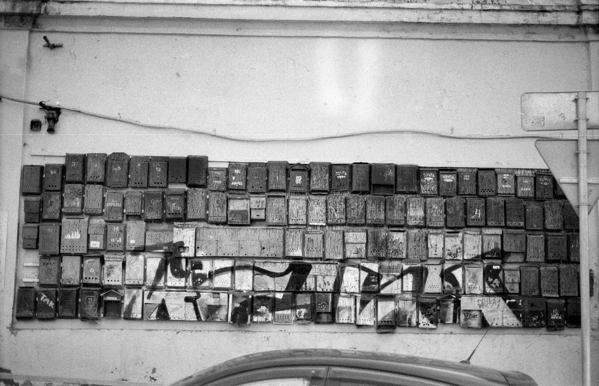 Black and white image of old, rusty mailboxes on a graffiti-covered wall, adding an urban rustic feel.