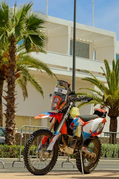 Vibrant motocross bike with number 129 parked amidst palm trees in an urban setting, capturing a tropical adventure vibe.
